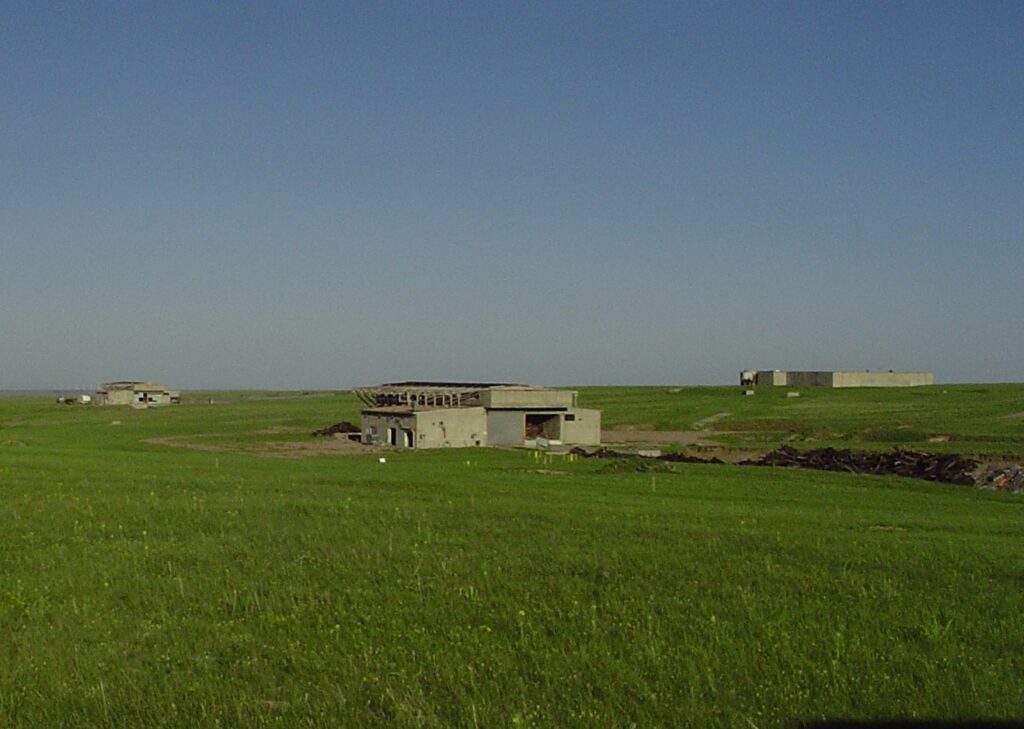 Photograph 1. The former Atlas “D” Missile Site 4 looking southeast, with Launch and Service Building 1 in the foreground. The missile control building is visible at right in the background and LSB 3 is in the background at left.