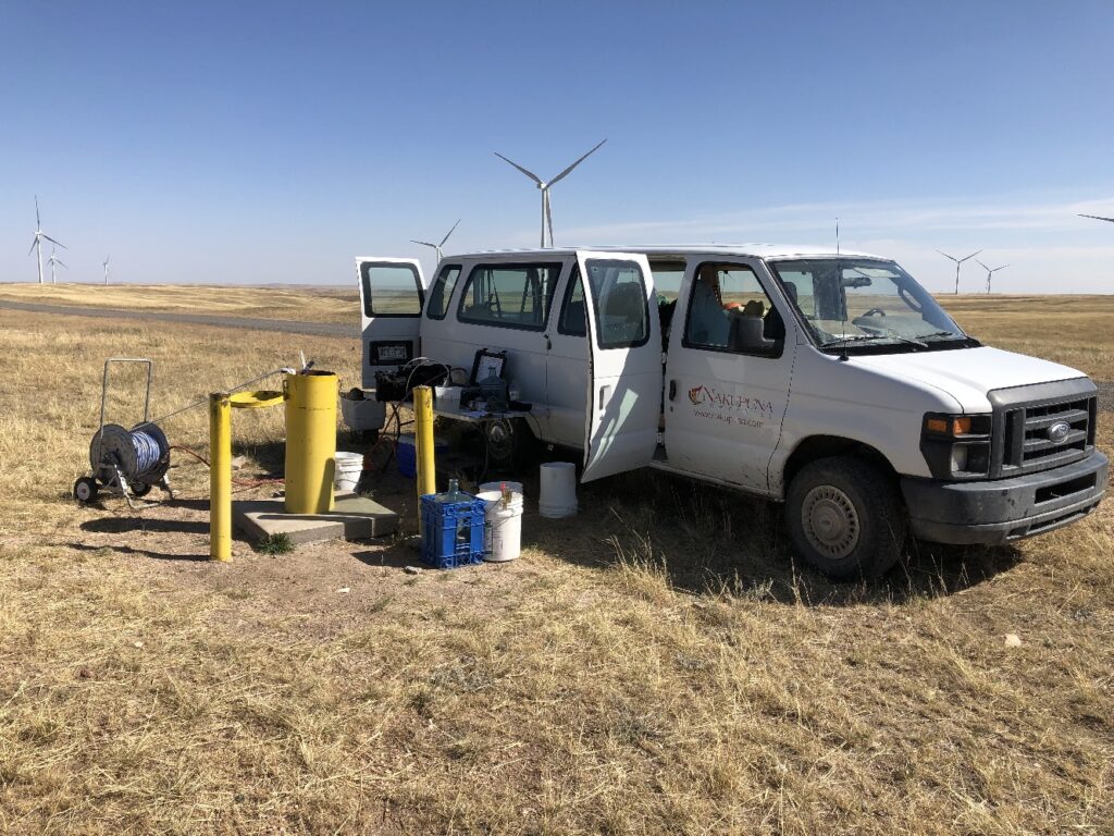 Photograph 8. The nested monitoring well MW92 is located at the east end of the Transition Area. A bladder pump is used to collect samples from the deeper-screened wells installed in the WRF. Several of the wind turbine that have been installed on the Belvoir Ranch are visible in the background. View is to the southeast.